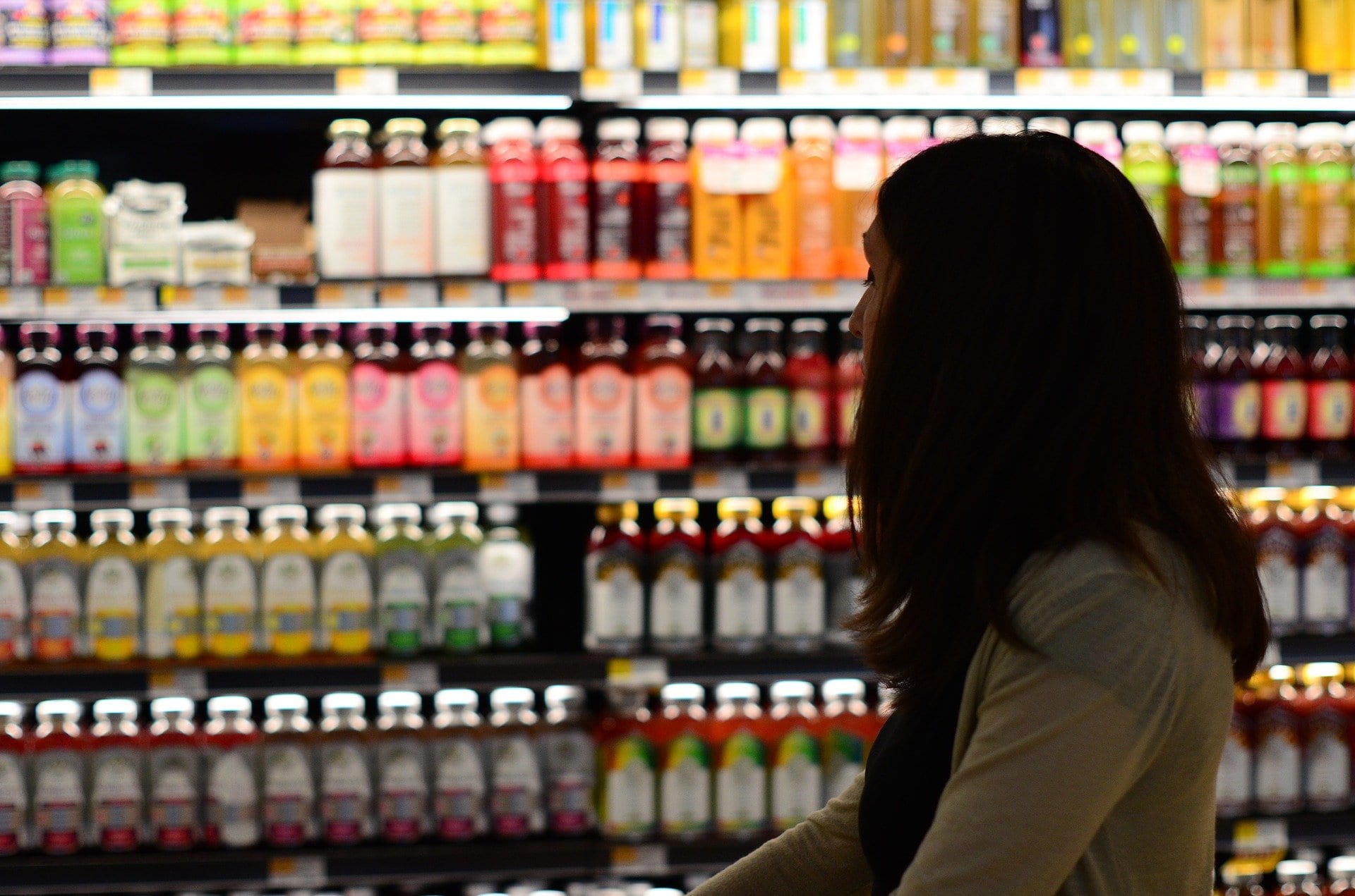 Woman silhouetted against colorful FMCG bottles on shelves; Sales Force Automation Software.